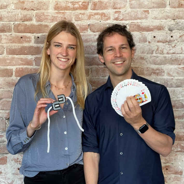 Links onderzoeker Anne Versluis die een touwgocheltruc vast heeft. Rechts illusionist Victor Mids die een waaier van speelkaarten in zijn hand heeft.