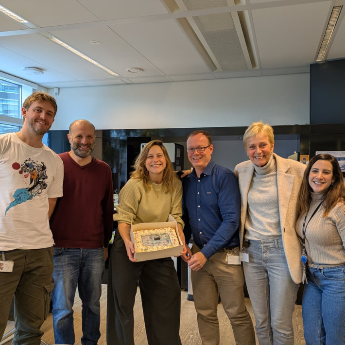 groepsfoto van de onderzoekers die een taart vasthouden. Op de taart staat een afbeelding van de wetenschappelijke publicatie