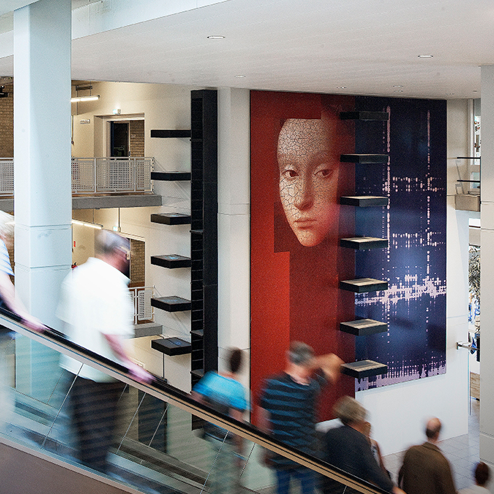 Roltrappen in de centrale hal met een groot kunstwerk op de muur.
