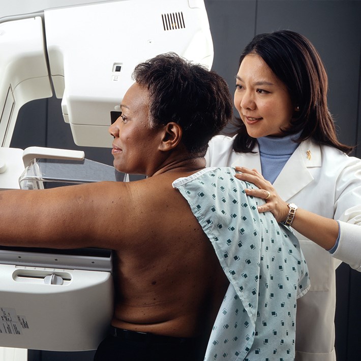 Medewerker begeleid patiënt bij mammogram.