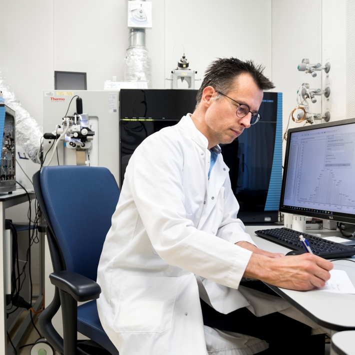 Researcher in lab coat behind computer screen in lab