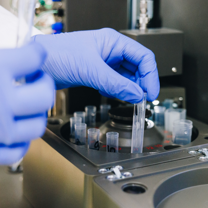 Close-up of researcher with white labcoat and blue rubber gloves putting test tubes into machine in lab