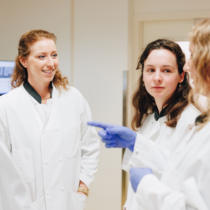 A group of researchers in white labcoats talk amongst each other