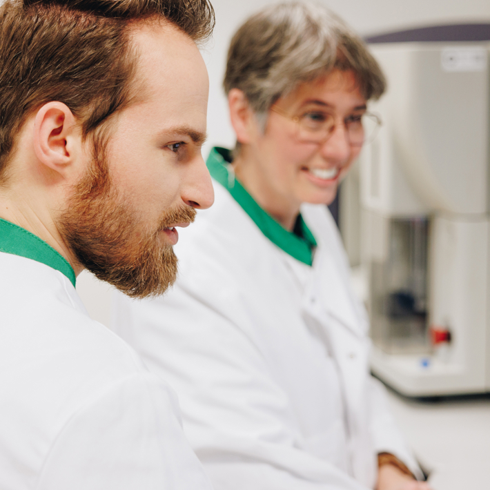 Two reseachers in front of lab equipment looking to something to the right of the image