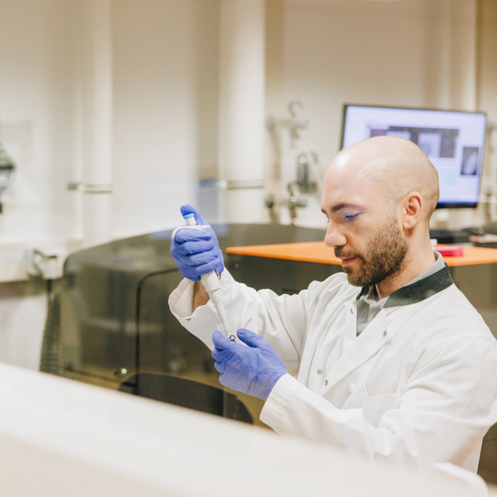Researcher pipetting in lab, seen from behind glass