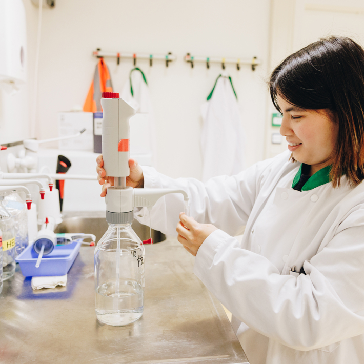 Researcher in white labcoat pipettes clear fluid in research lab