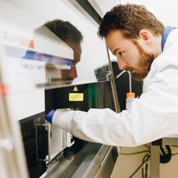 Researcher in white labcoat with rubber gloves uses lab equipment with extractor hood