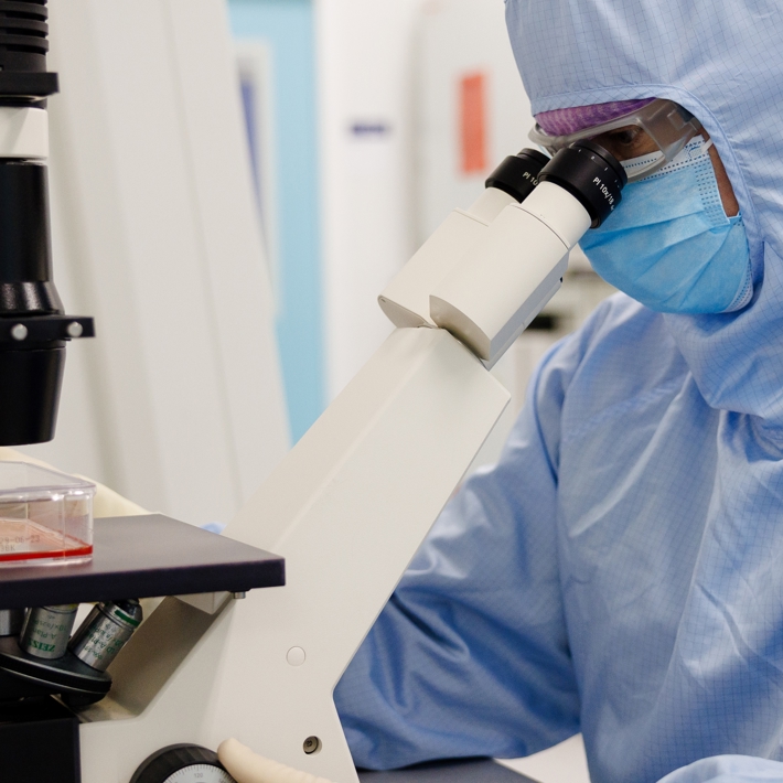 Person sitting behind microscope and looking through oculars in cleanroom